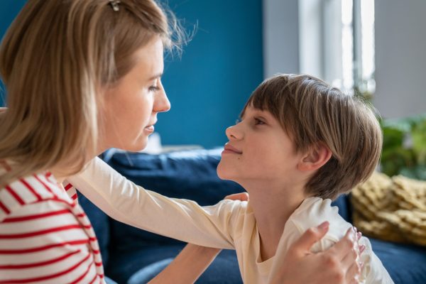 Mother-son bond. Young woman mom looking tenderly at child son while sitting together on sofa, loving mum parent and boy kid looking into each others eyes, staying connected. Love and childcare